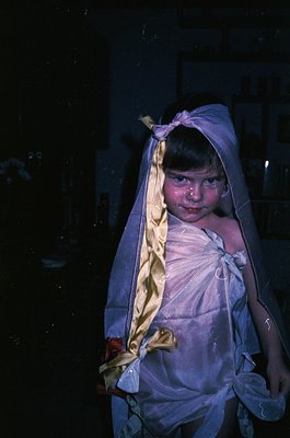 Vintage black-and-white portrait of a child wrapped in a sheer veil, likely for a religious or cultural ceremony. The headsca...