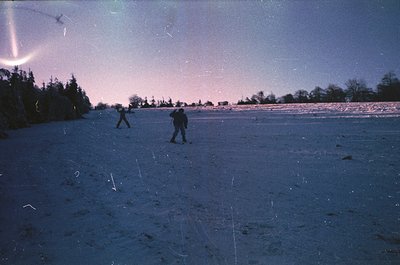 Vintage black-and-white photo of three skiers gliding across a snow-covered plain under a faintly illuminated sky, likely 196...