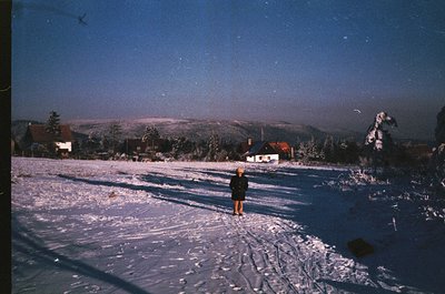 Vintage ski slope under twilight, featuring a lone figure in winter gear. Snow-covered terrain with ski tracks, framed by for...