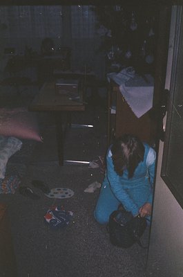 Vintage interior shot of a dimly lit bedroom with mid-century furnishings. A person in blue track pants kneels on patterned l...