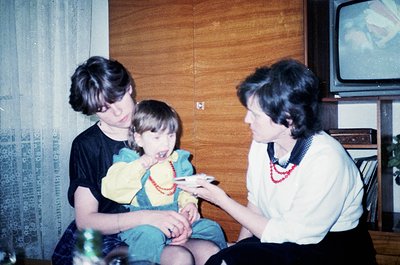 Vintage indoor family moment: two adults and a child seated on a sofa, sharing a snack. The woman wears a white blouse with r...