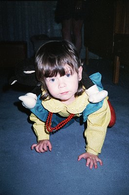 Young child in vintage-style outfit (yellow knit sweater with green collar, red beaded necklace) crawling on dark floor, hold...