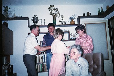 Vintage indoor gathering in a mid-century living room with built-in shelving displaying decorative items like vases, trophies...