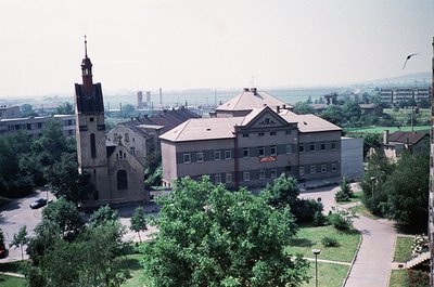 Aerial view of a historic church with a tall brick steeple and arched entrance, adjacent to a mid-20th-century institutional ...