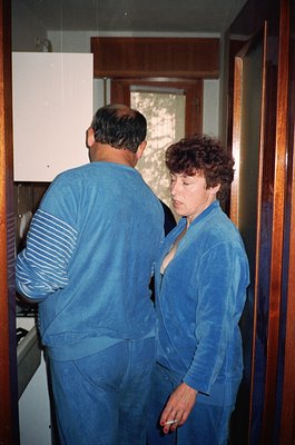 Couple in matching blue tracksuits examining a vintage analog watch, likely 1980s-1990s. Indoor setting with wooden paneling ...