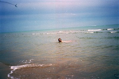 Vintage seaside shot of lone swimmer in calm ocean waves, mid-20th century. Soft focus and muted tones suggest analog film. G...