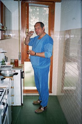 Mid-century kitchen interior with white stove, white tiles, and green linoleum flooring. Man in striped blue sweater and beig...