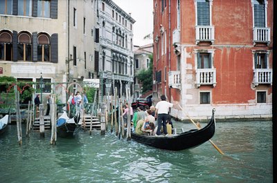 Venetian canal scene with traditional gondolas and historic buildings. Wooden poles line the waterfront, supporting wooden wa...