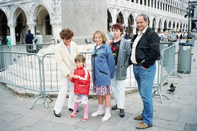 Family group photo in Piazza San Marco, Venice, Italy, 1980s. Four adults and a child pose in front of Gothic arches and meta...