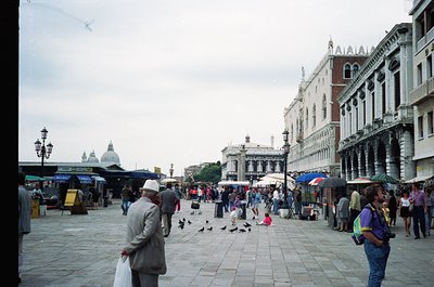 Vibrant Piazza San Marco, Venice, Italy—crowded with tourists and pigeons under overcast skies. Gothic architecture frames th...