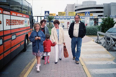 Family group walks near a **Residentur** coach labeled for Hamburg/Berlin, 1990s European travel hub. Signage includes curren...