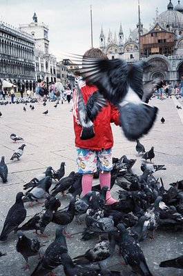 Child feeding pigeons in St. Mark’s Square (), Venice, Italy. Mid-20th century urban scene with historic Venetian architectur...
