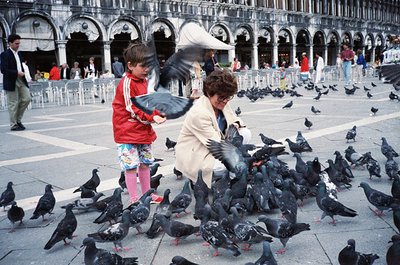 A woman and child feeding pigeons in St. Mark’s Square (), Venice, Italy. The 1970s-era scene captures iconic Venetian archit...