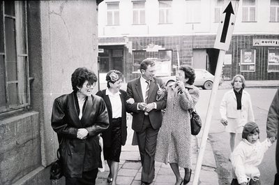 Mid-20th century street scene featuring a group of adults and a child in formal attire, likely 1960s–1970s. Men and women in ...