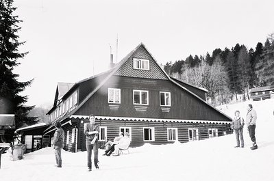 Classic alpine lodge with timber-framed architecture, snow-covered roof, and decorative scalloped trim. Group of winter sport...