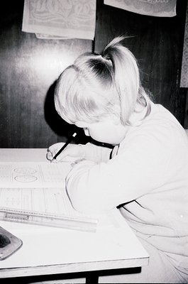 A young girl in a 1960s-style blouse focuses intently on drafting with a pencil and ruler on a technical drawing. Mid-century...