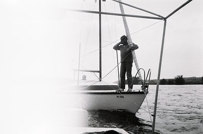 Black-and-white shot of a sailor adjusting a sail on a classic sailboat, marked "PS STIR." Mid-20th century maritime attire a...