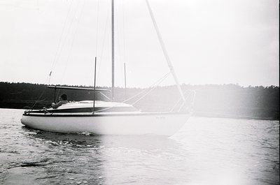 Classic monochrome sailboat cruising on calm waters, likely Baltic Sea or Nordic region. Single person at helm, mid-20th cent...