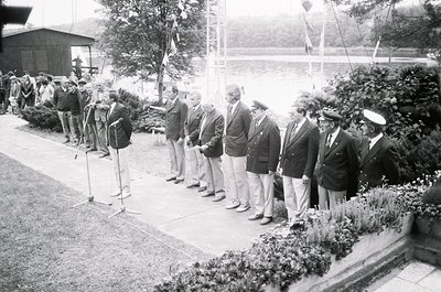 Black-and-white formal gathering of uniformed men in outdoor ceremony, likely mid-20th century. Men in suits, military caps, ...