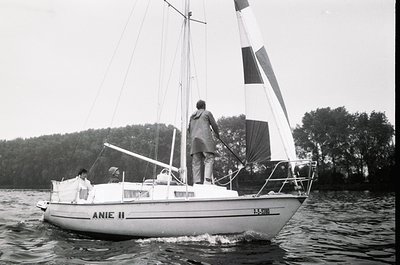 Classic 1970s sailboat "Anie II" cruising on calm waters, with two individuals aboard. The vessel features a white hull, tall...