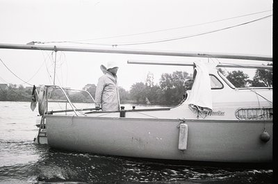 Classic mid-20th century sailboat with "Nautilus" branding, moored on calm waters. Person in vintage sailing attire (hat, jac...