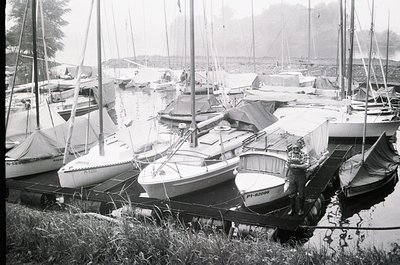 Docked vintage sailboats in a marina, likely mid-20th century. Classic fiberglass hulls with simple rigging and covered cockp...