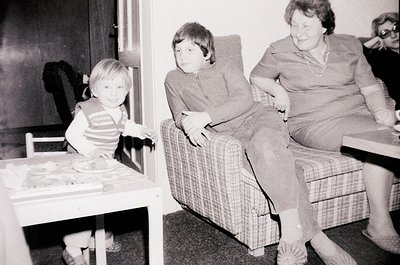 A mid-20th century indoor scene: two children and an adult woman in a modest living space. The boy in striped shirt stands by...