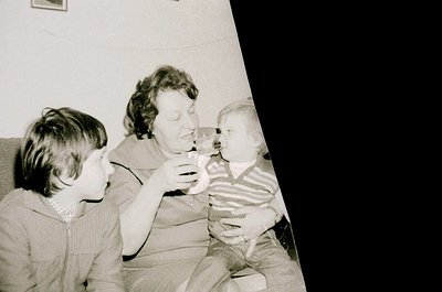 Black-and-white snapshot of three generations: a woman in mid-20th-century dress holding a baby, with a young boy leaning in....