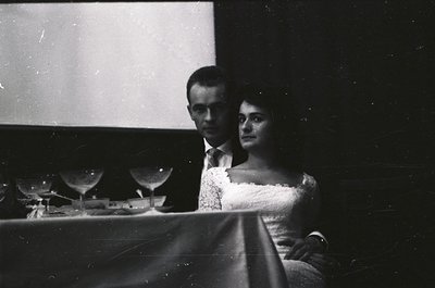 Black-and-white portrait of a man and woman seated at a piano, likely from the 1940s–1960s. The man wears a suit with a white...