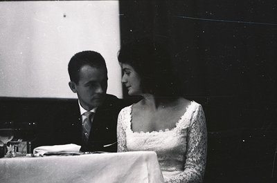 Couple seated at a formal table, likely at a 1960s-1970s wedding or gala. Man in dark suit, woman in lace wedding dress. Indo...