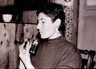 Vintage black-and-white portrait of a person examining a vintage camera, likely a Leica-style rangefinder. Indoor setting wit...