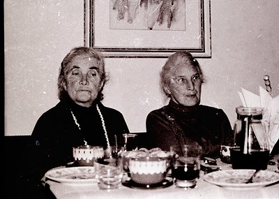 Two elderly women seated at a formal table, likely mid-20th century (1950s–1960s). Table setting includes vintage china, a te...