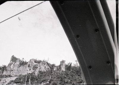 Black-and-white aerial view of rugged limestone formations and dense foliage, likely part of a historic or archaeological sit...