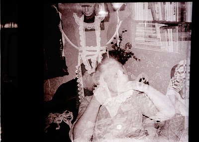 Vintage sepia-toned photo of a seated woman in a lace-trimmed dress, holding a floral arrangement. Partial view of another fi...