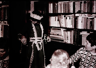 Vintage black-and-white photo of a theatrical performance in a dimly lit room. Central figure wears a dramatic, lace-trimmed ...