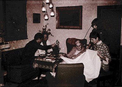 Vintage sepia-toned indoor scene featuring three women in a modestly furnished room, likely mid-20th century. A seated elderl...