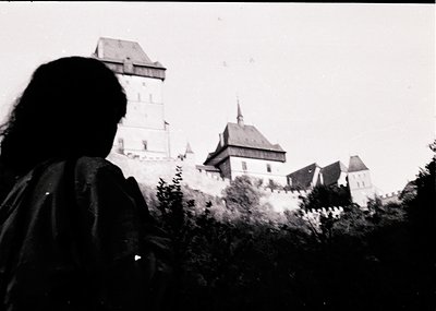 Silhouetted figure frames medieval castle with steep-turreted towers and gabled roofs, likely štejnCastle (). Black-and-white...