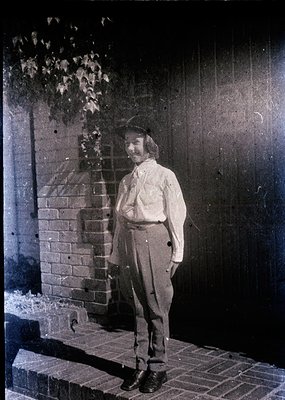 Vintage sepia-toned portrait of a man in early 20th-century attire—wide-collared shirt, high-waisted trousers, and a fedora—s...