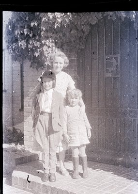 Vintage sepia-toned family portrait from early 20th century, likely 1910s–1920s. Woman in high-necked blouse and long skirt p...