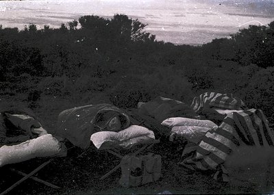 Vintage sepia-toned photograph of a battlefield scene with discarded military gear and equipment. Visible are helmets, cantee...