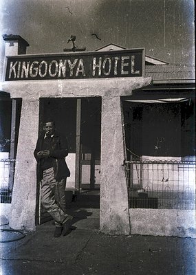 Black-and-white photo of a man in 1960s-era attire posing under the "Kingoonya Hotel" sign. Concrete columns frame the entran...