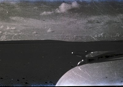 Vintage aerial photo of a coastal landscape with low-lying clouds and mist. The horizon reveals a dark shoreline with subtle ...