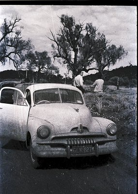 Vintage 1950s-era sedan (likely a Studebaker) with chrome grille and round headlights, parked on a rural road. Two men in lig...
