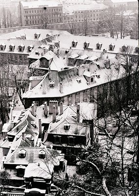 Snow-covered rooftops of a densely packed European cityscape, likely 1950s–1970s. Distinctive gabled architecture with chimne...