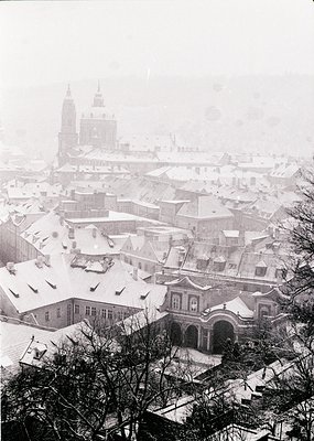 Snow-covered rooftops and historic architecture in a European cityscape, likely . Prominent Baroque-style buildings and a cat...