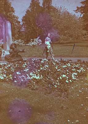 Vintage sepia-toned photograph of a lone figure in a wide-brimmed hat and patterned dress, walking on a dirt path surrounded ...