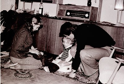 Vintage black-and-white indoor scene: three individuals (two adults, one child) playing with a cat on a patterned rug. Adults...