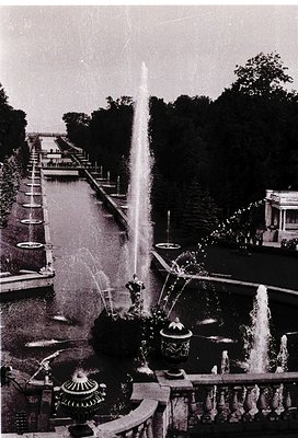Symmetrical canal flanked by tiered fountains and ornate planters, likely part of a grand European palace or park. Mid-20th c...