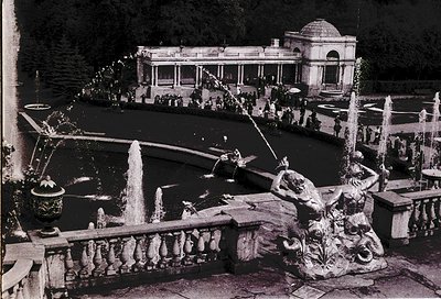 Vintage black-and-white photo of an ornate **fountain courtyard** with classical sculptures and cascading water. Central **tr...