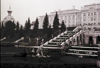 Vintage black-and-white view of grand **staircase cascading into tiered pools**, flanked by classical architecture and conife...